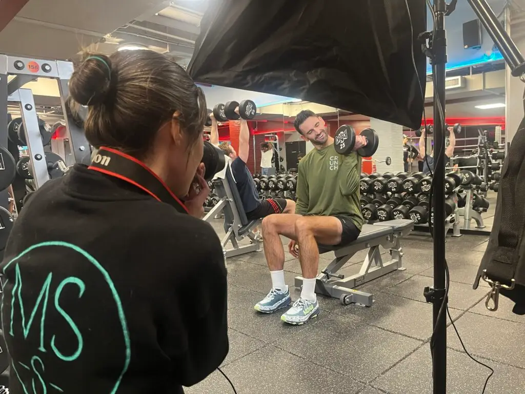 Angle over the photographer's shoulder to see Carl Radke checking out dumbbell he's lifting under strobe lights