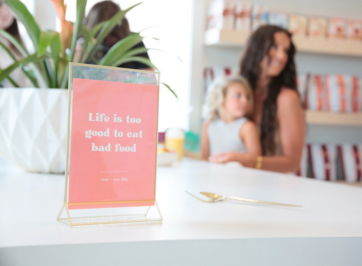 sign says life is too good to eat bad food as mom wait with little girl in bright store