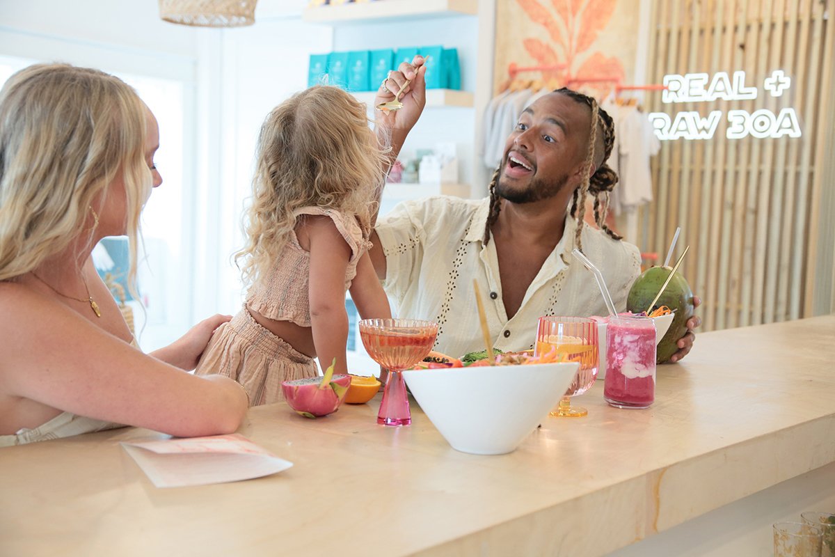 dad spoons food into toddlers mouth at bar in sunlight drenched setting