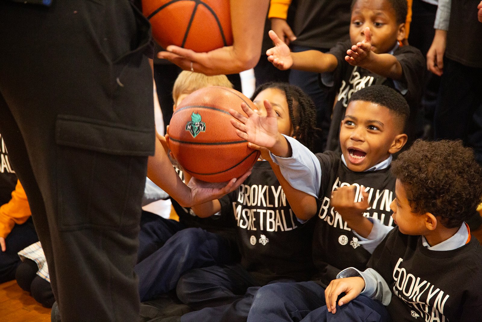 young boys in Brooklyn Basketball shirts stretch out their hands to receive basketballs