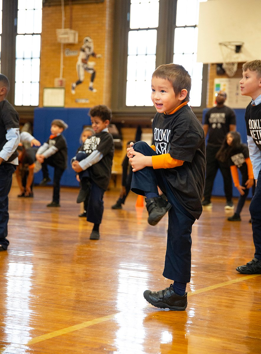 boy balances on one leg while bringing knee to chest