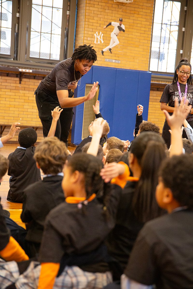 Brooklyn Basketball woman high fives one scholar while other raise hands
