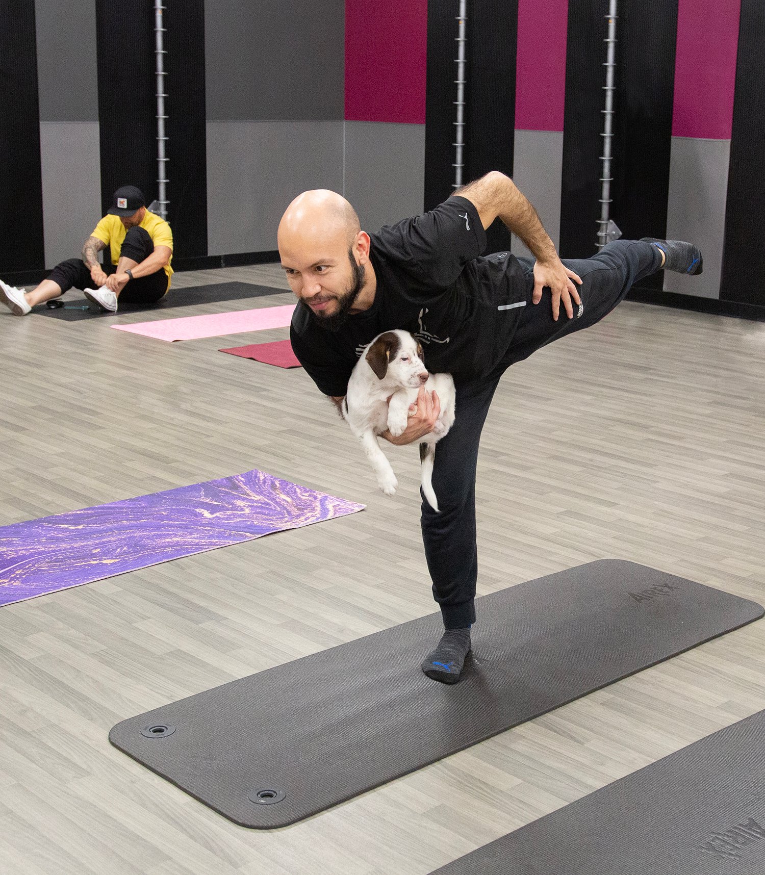 man balances on one leg with other leg extended behind him like an arabesque while cradling puppy