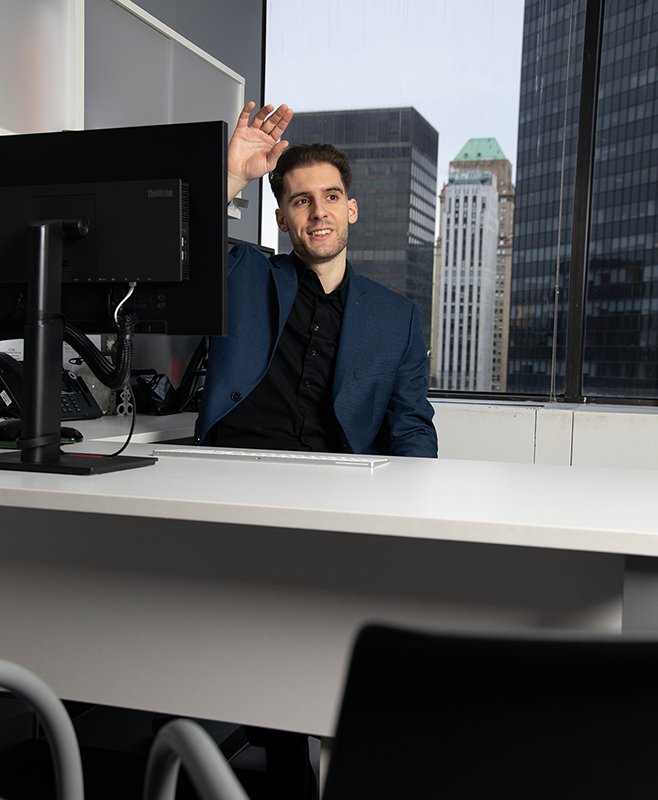 man at desk waves to someone maybe in hallway